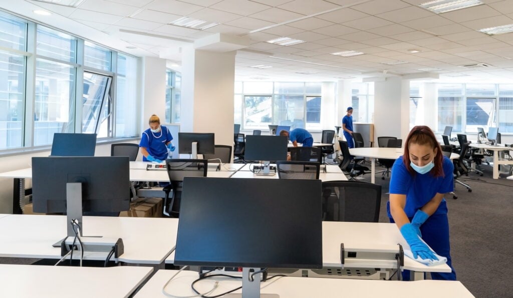Professional cleaners with the masks on their faces clean and disinfect an empty office space