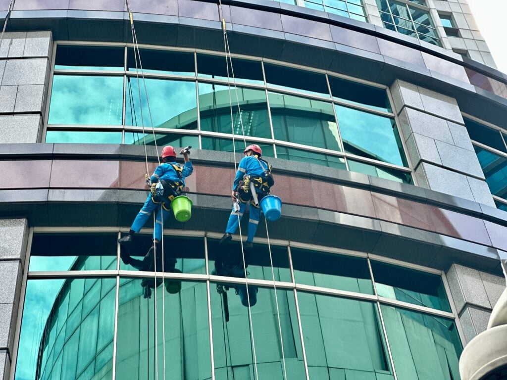 Two workers climbing to clean glass windows — a high-rise maintenance task that highlights the skill and risk involved in urban building upkeep. Tanah Abang, Jakarta - June 16, 2025